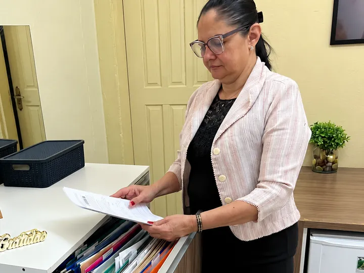 Suzane Salvador em pé junto ao arquivo do escritório, conferindo um documento